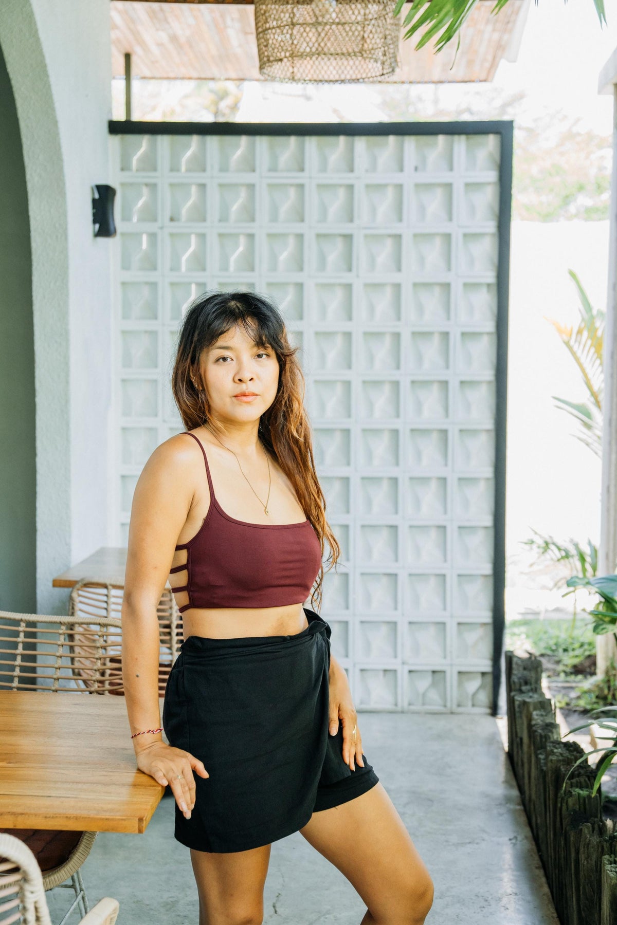 A woman posing on a patio wearing a burgundy crop top and black wrap-style shorts.